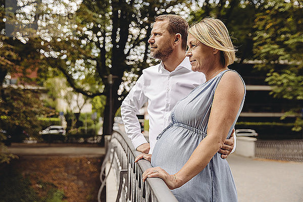 Mature pregnant couple standing at bridge in park