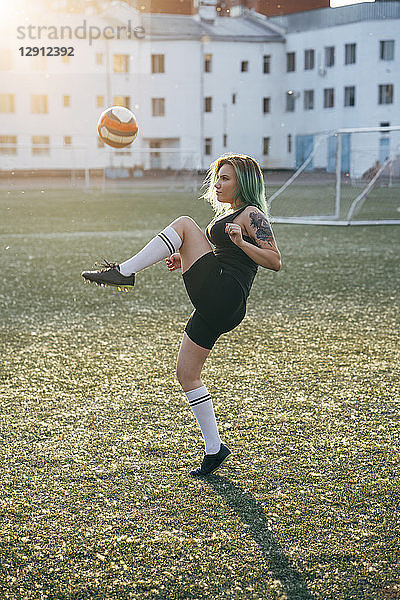 Young woman playing football on football ground balancing the ball