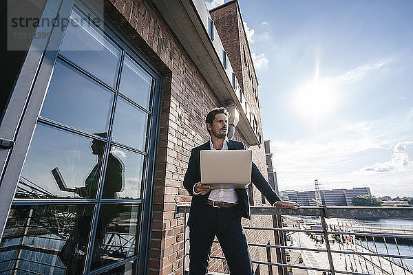 Businessman standing on balcony  using laptop