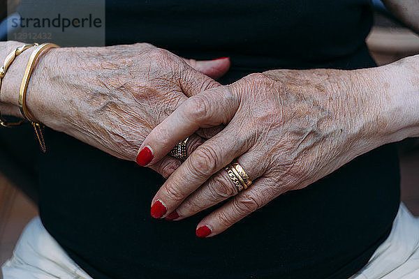 Hands of senior woman with golden rings and red painted nails