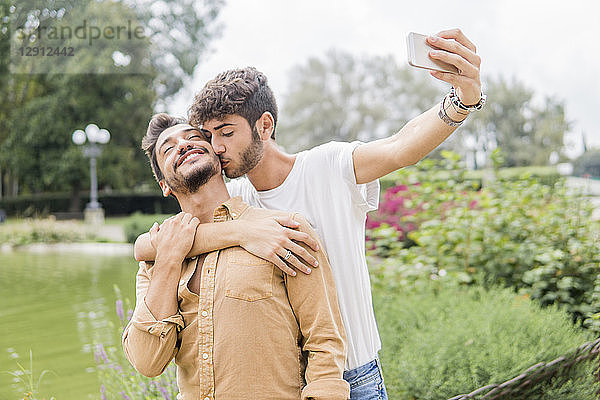 Happy young gay couple taking selfie with smartphone at city park