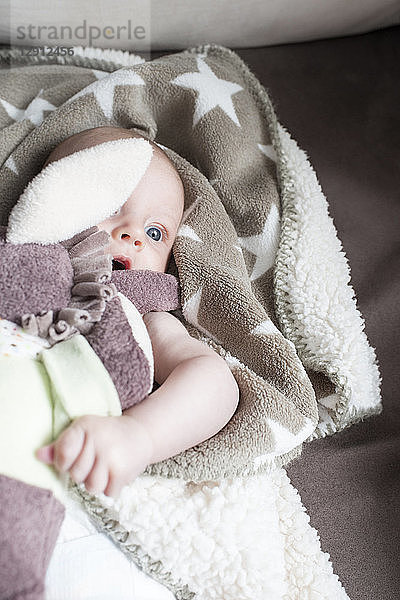 Portrait of baby girl wrapped in blanket lying on a couch