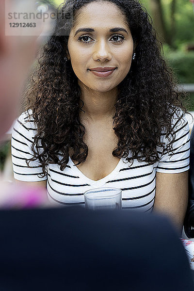 Portrait of a young woman sitting in beer garden  looking at a friend
