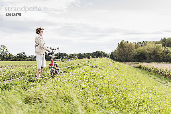 Senior woman with bicycle in rural landscape