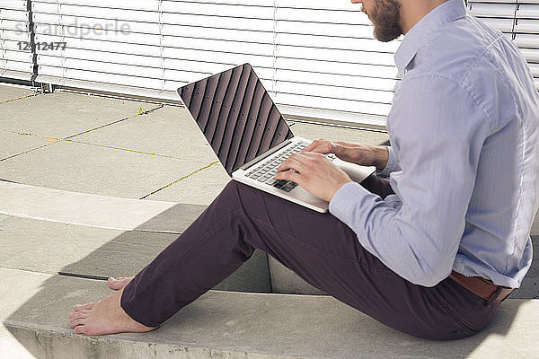 Barefoot businessman using laptop outdoors