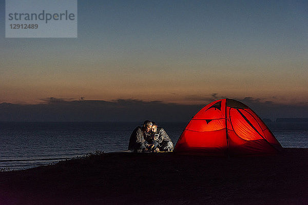 Romantic couple camping on the beach  using smartphone
