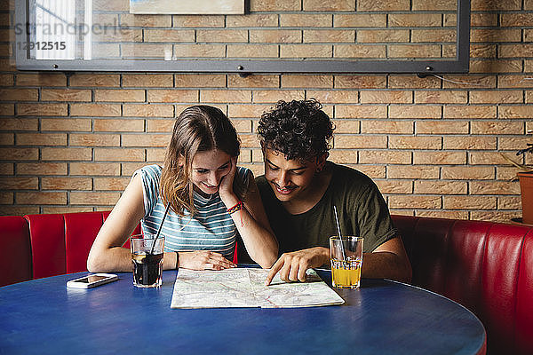 Smiling young couple sitting at table in a cafe with map