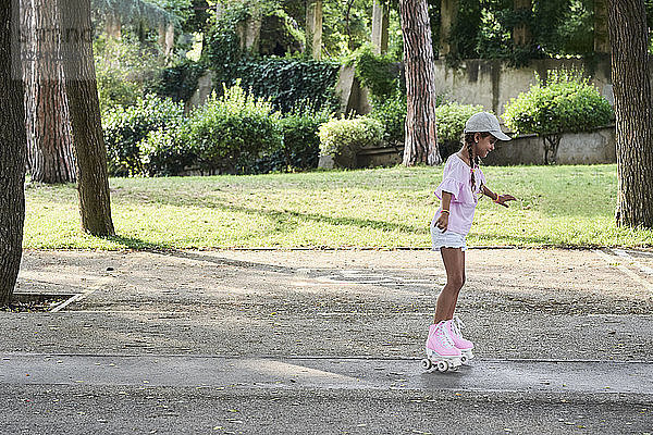 Little girl wearing braids and cap roller skating in the park