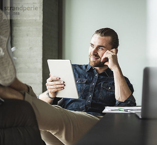 Businessman sitting in office with feet up using tablet