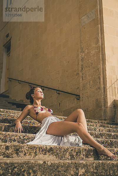 Teenage girl weraing long skirt and bikini top  posing on stairs