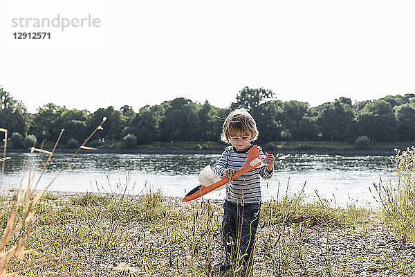 Boy playing with a toy plane at the riverside