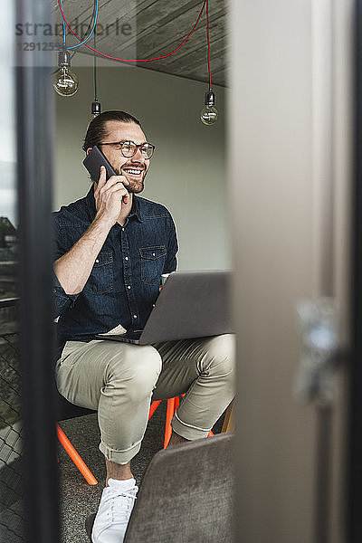 Smiling young businessman on cell phone in office