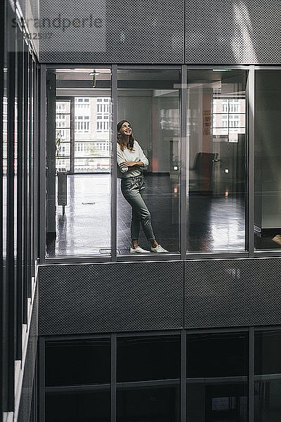 Woman standing at office window  looking up  smiling