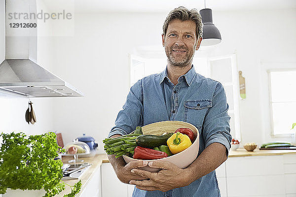 Mature man standing in kitchen  holding a bowl with vegetables