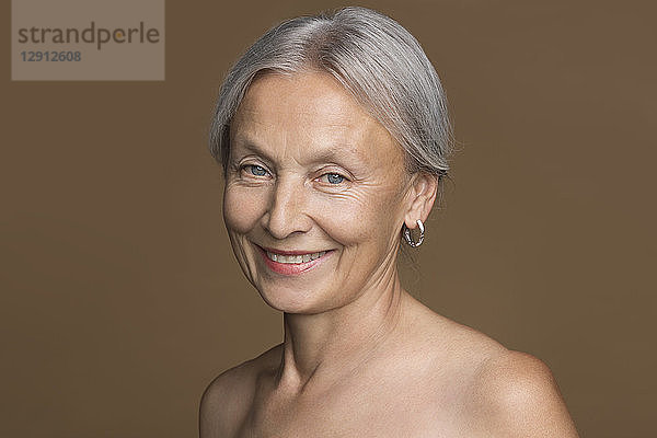 Portrait of naked senior woman with grey hair in front of brown background