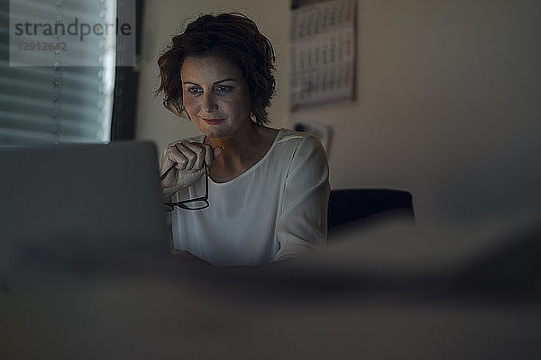 Businesswoman working overtime  using laptop  holding glasses