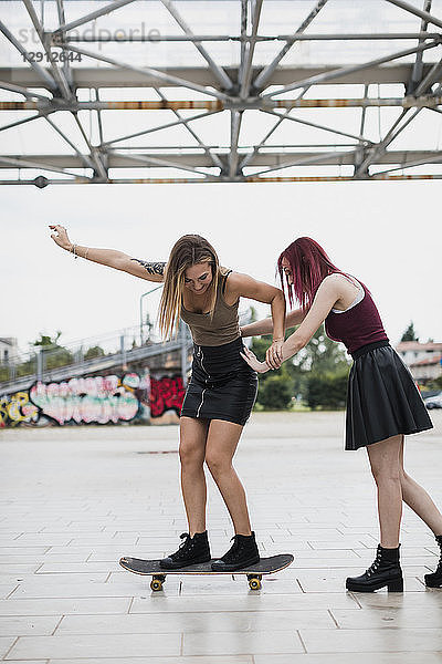 Young woman pushing friend on skateboard in the city