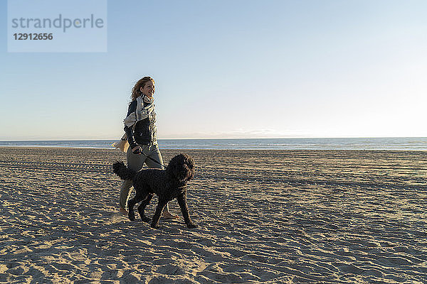 Young woman walking on the beach with her dog