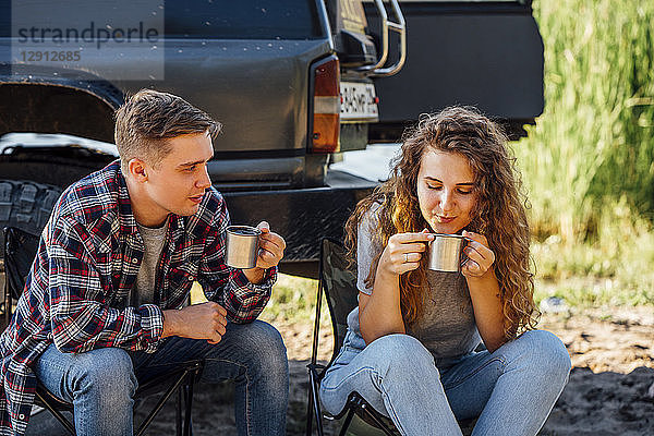 Young couple sitting by car  taking a break  drinking tea