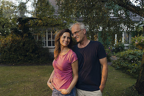 Smiling mature couple standing in garden of their home