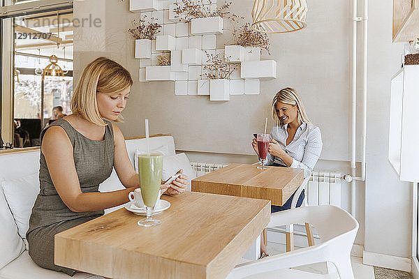 Two young women using smartphones in a cafe