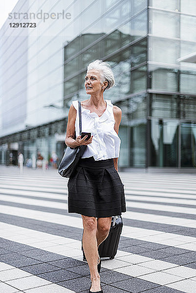 Senior woman with cell phone and baggage on the move