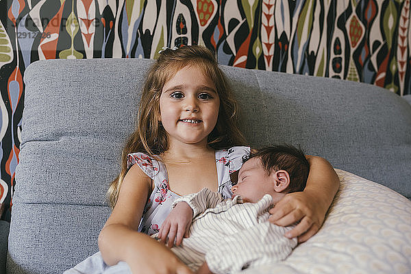 Smiling girl sitting on couch holding newborn baby brother