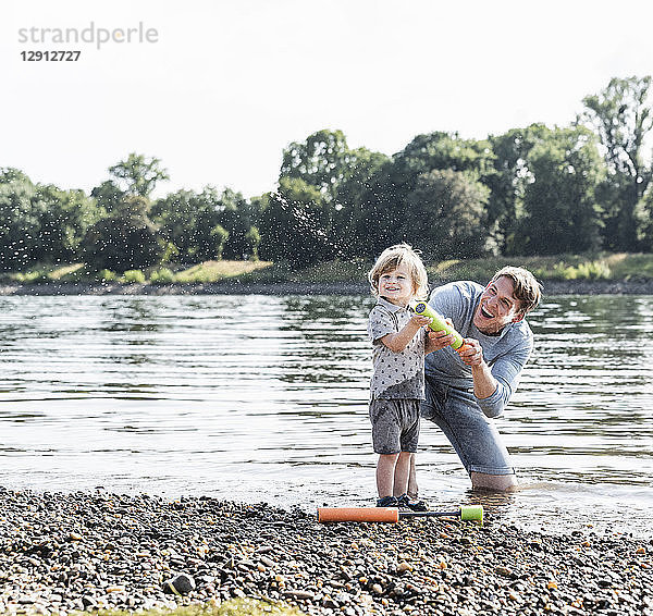 Father and son having fun at the riverside  playing with a water gun