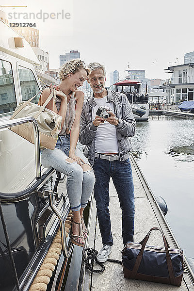 Older man with camera and young woman standing with travelling bags on jetty next to yacht