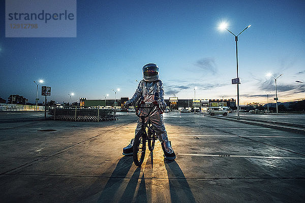 Spaceman in the city at night on parking lot with bmx bike