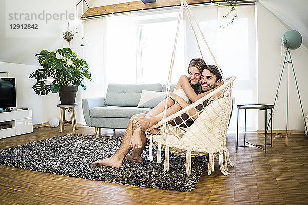 Happy affectionate couple sitting in hanging chair at home