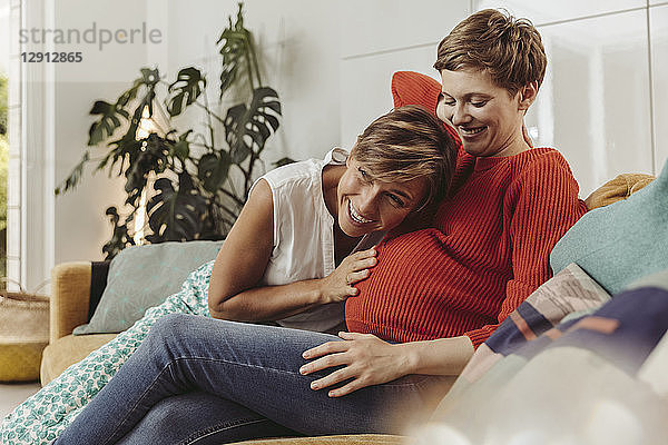 Happy lesbian couple feeling movements of baby belly of the expectant mother