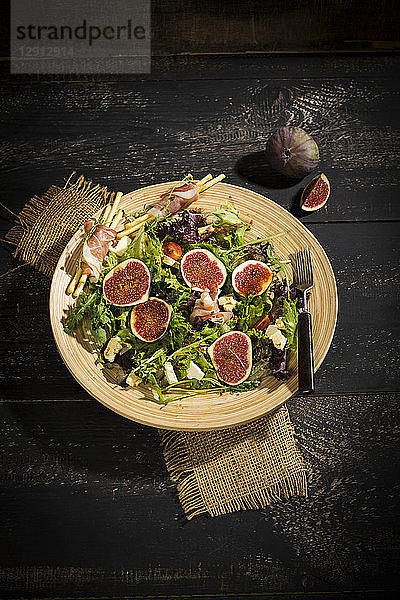 Mixed salad with figs  tomatoes  sheep cheese  grissini with ham on bambus plate