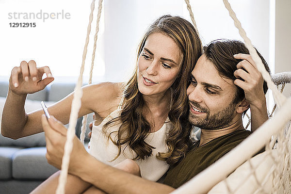 Couple in hanging chair at home looking at tablet