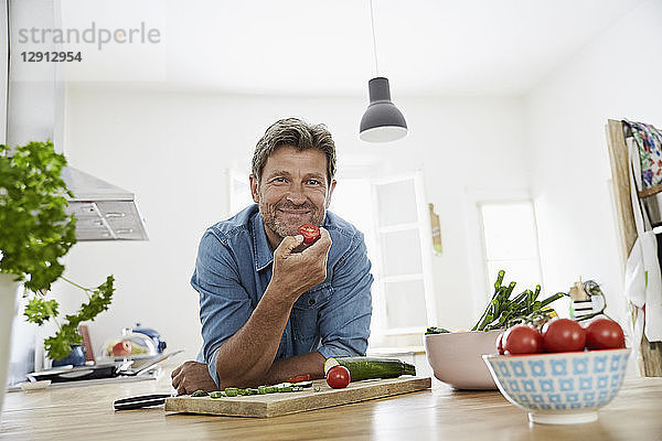 Mature man in his kitchen eating tomato