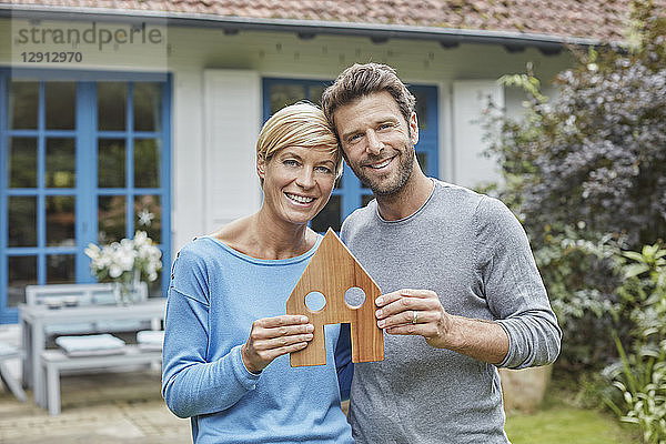 Portrait of smiling couple standing in front of their home holding house model