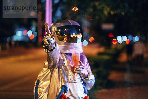 Spaceman in the city at night with takeaway drink making victory gesture