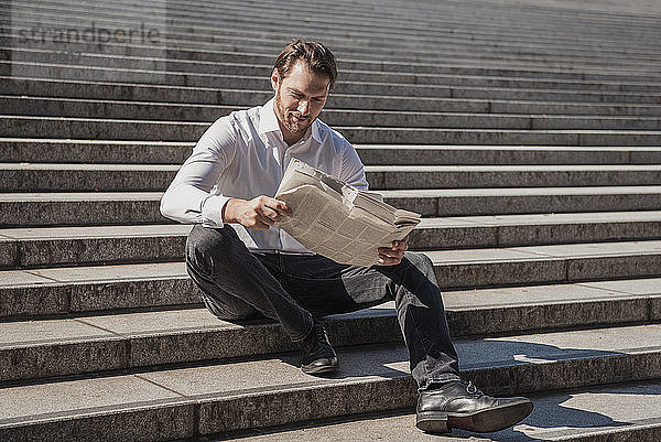 Smiling businessman sitting on stairs reading newspaper