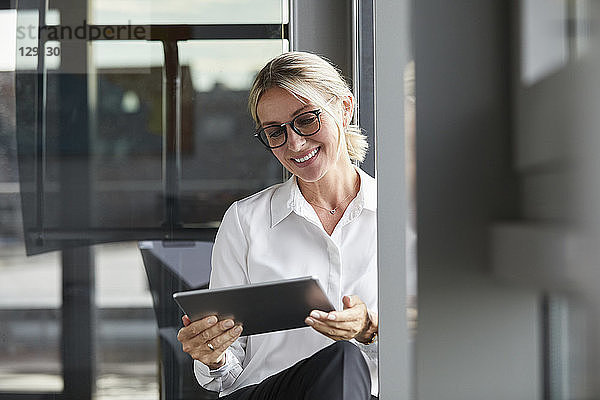 Serene businesswoman sitting on ground in office  using digital tablet