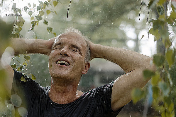 Smiling mature man enjoying summer rain in garden