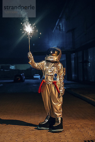 Spaceman standing outdoors at night holding sparkler