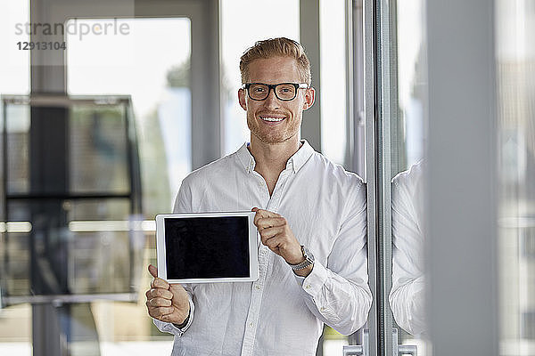 Portrait of smiling businessman showing tablet at the window in office