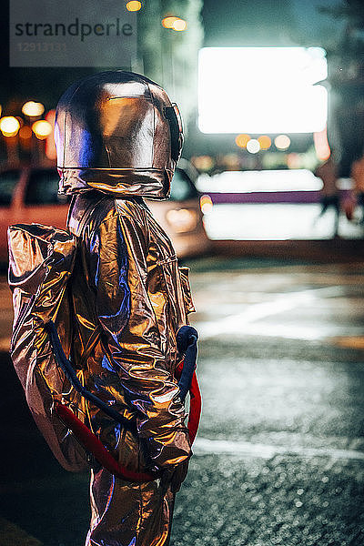 Spaceman on a street in the city at night attracted by shining projection screen