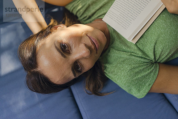 Portrait of smiling mature woman lying on couch at home with book