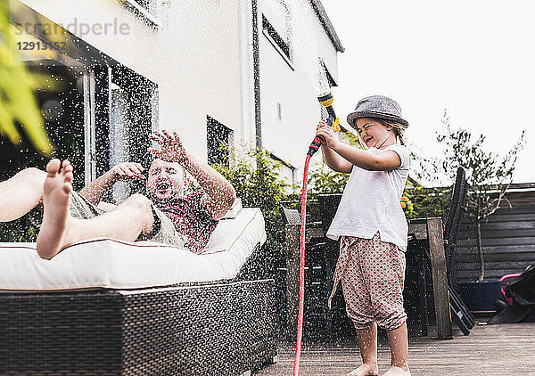 Fathercand daughter in the garden  daughter splashing water with hose