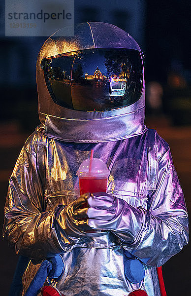 Spaceman in the city at night with takeaway drink