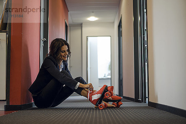 Mature businesswoman sitting in office corridor  putting on roller skates