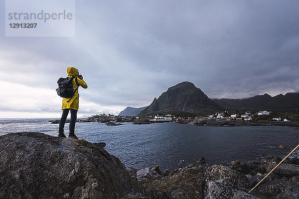 Norway  Lofoten  rear view of man standing on a rock at the coast taking a picture