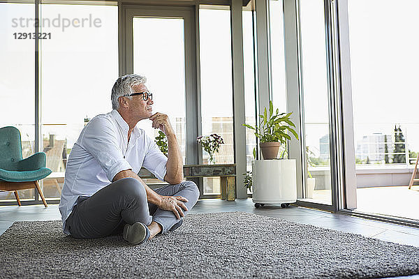 Pensive mature man sitting on carpet at home