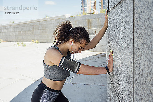 Young athletic woman listening to music leaning against a wall